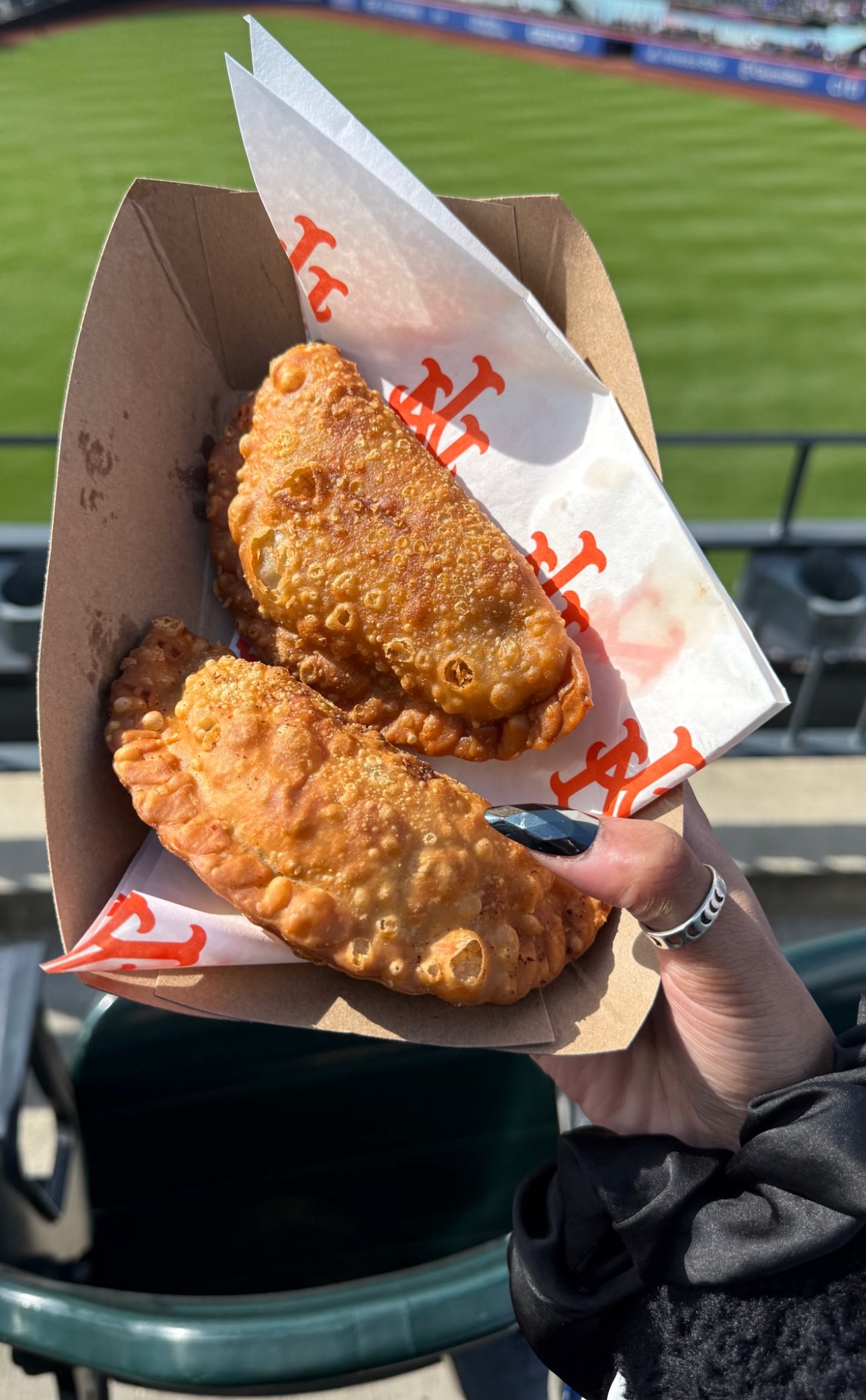 Two fried empanadas in a cardboard container with a paper sleeve at a sports event.